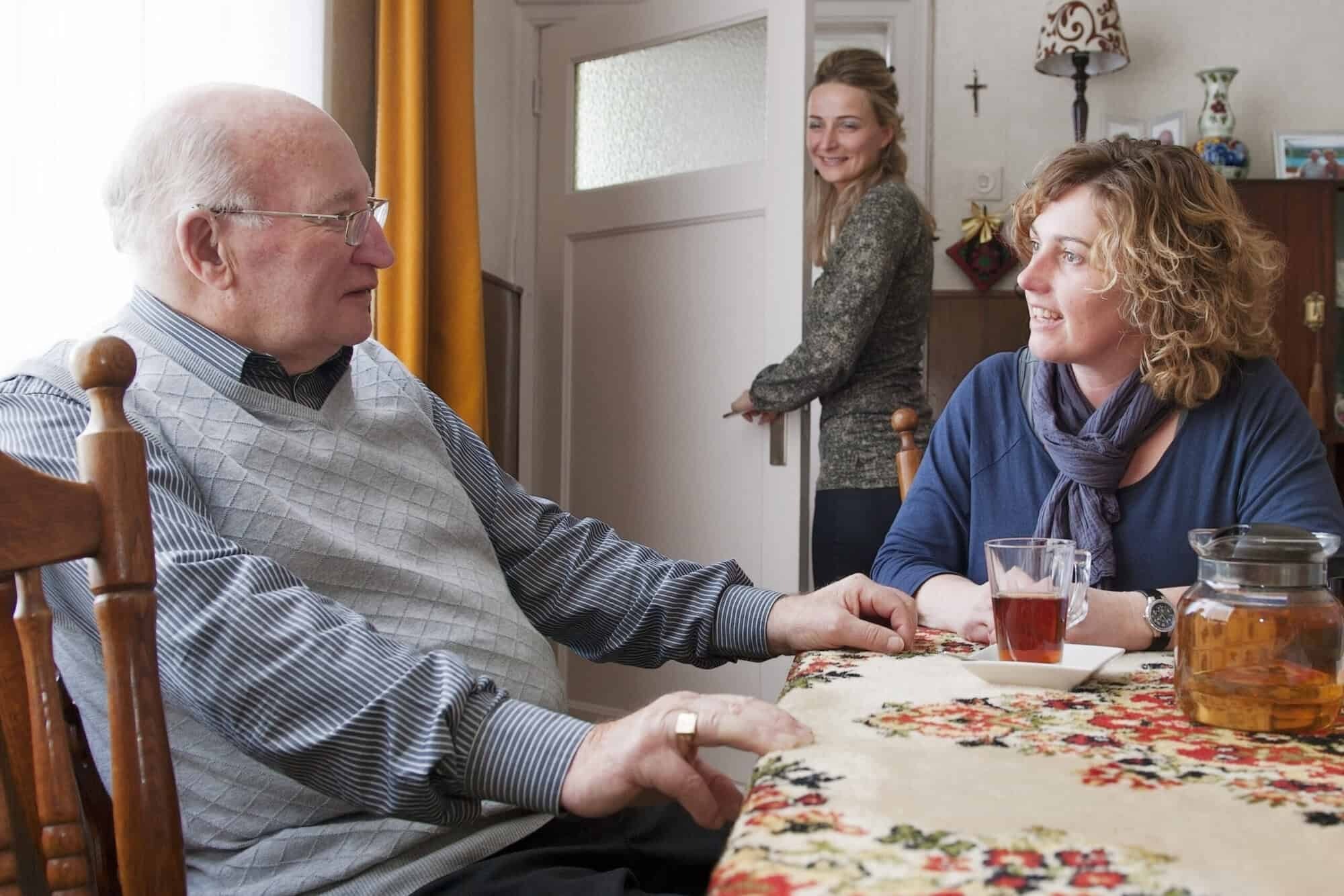 Oudere man in gesprek met zorgverlener aan de keukentafel – persoonlijke ouderenzorg en gezelschap aan huis in Midden-Brabant