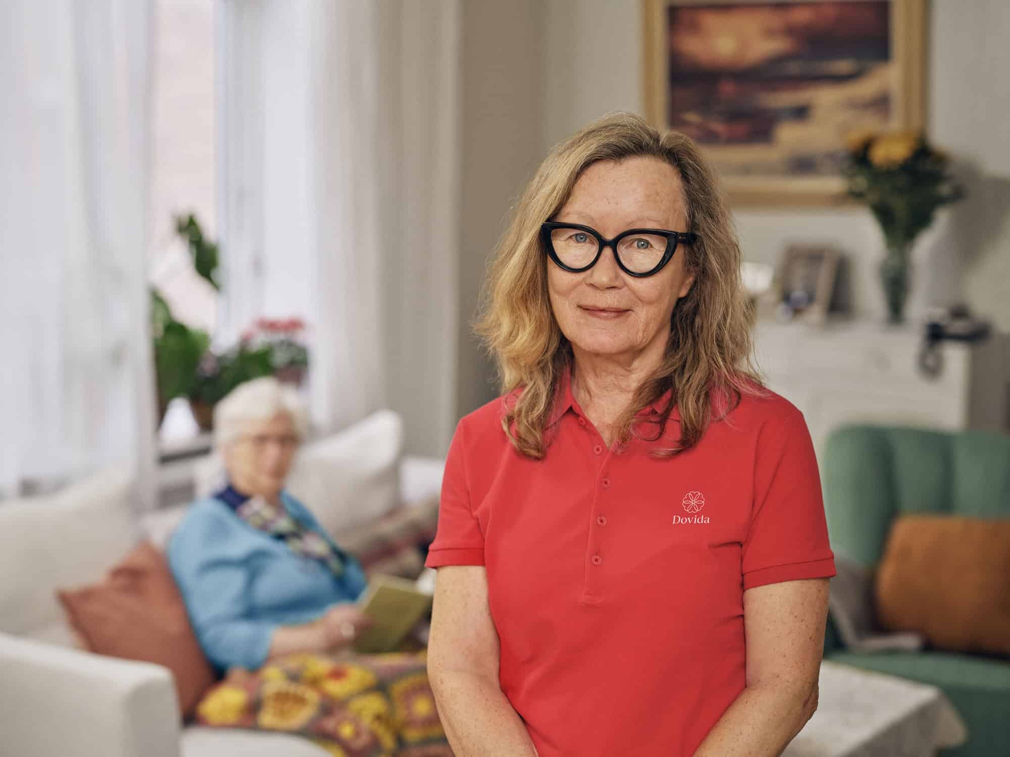 Een zelfverzekerde vrouw met bril en in een rood Dovida shirt lacht in haar thuiszorgkantoor en straalt professionaliteit uit 