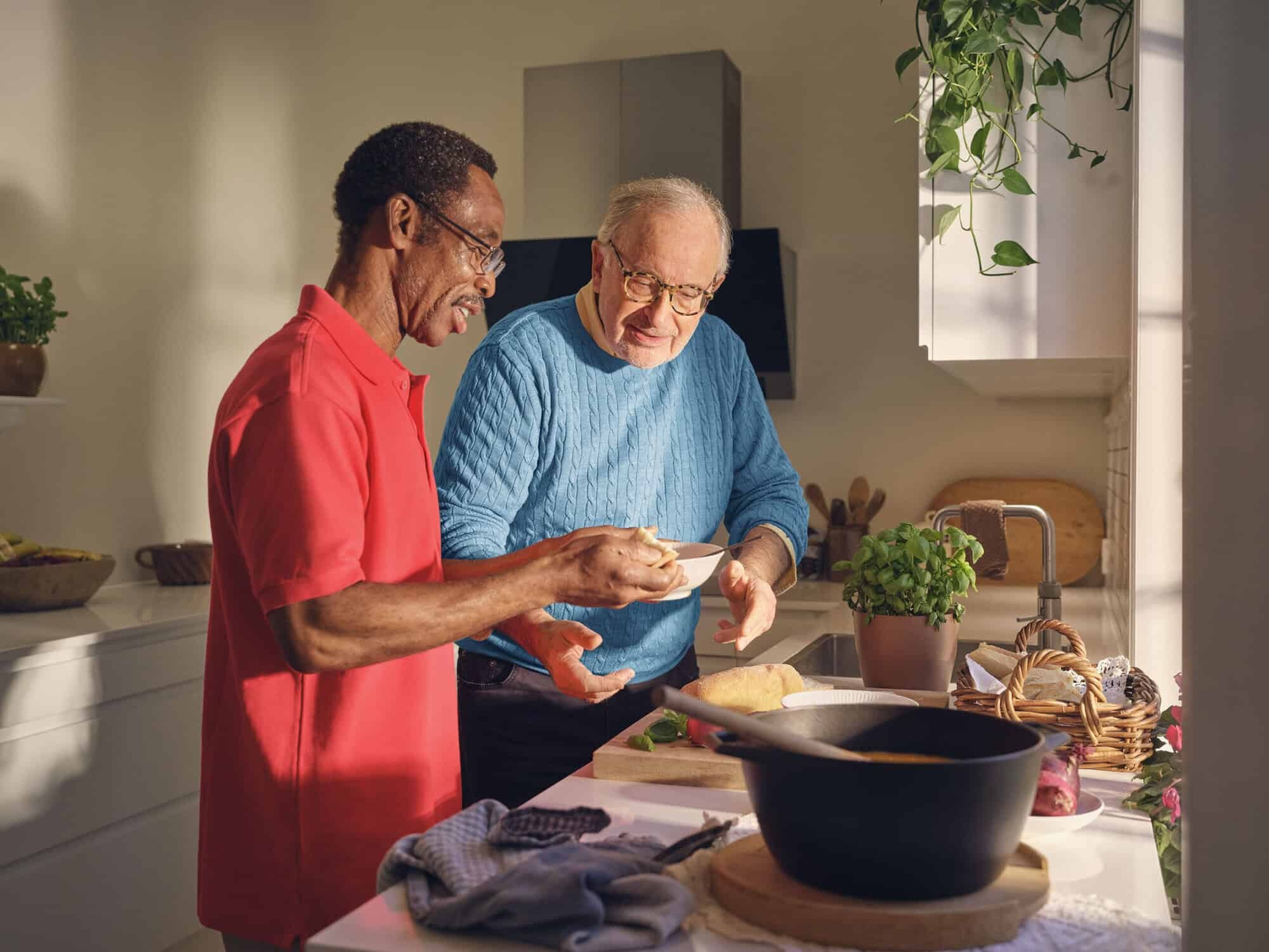 Twee mannen koken met plezier samen in een keuken en tonen daarmee de filosofie van de zorgcirkel door samen een maaltijd te bereiden. 