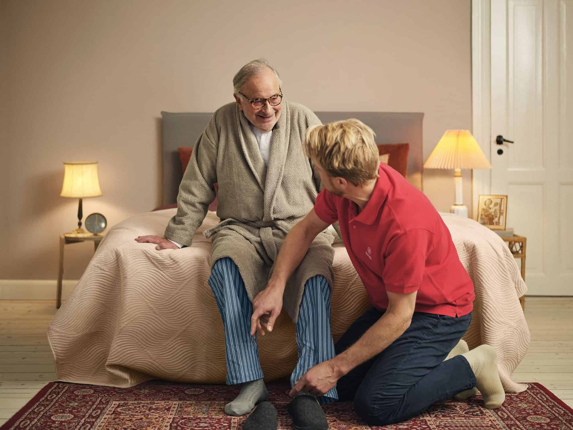 Een persoonlijke caregiver helpt een oudere man met het aantrekken van zijn schoenen en toont daarmee de essentie van thuishulpdiensten aan. 