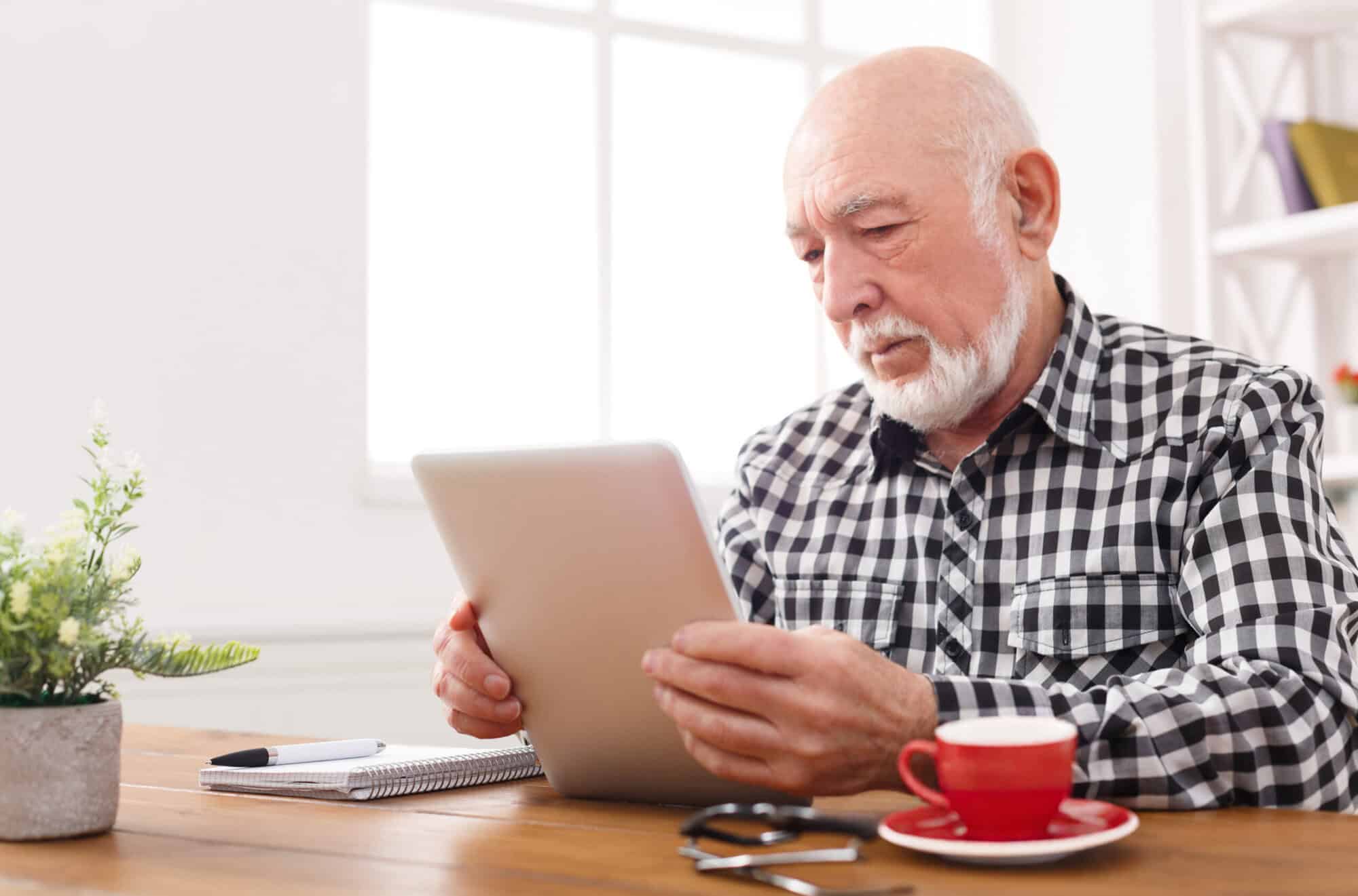 Senior man reading news on digital tablet